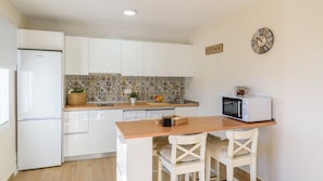 A compact kitchen with white cabinets, a tiled backsplash, a microwave, and a small dining table with chairs.