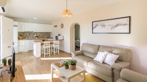Ein modernes Wohnzimmer mit einem beigen Sofa, einem Couchtisch mit Pflanzen und einer Küche im Hintergrund.