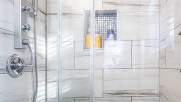 A modern shower with a glass door, marble tiles, and a handheld showerhead.
