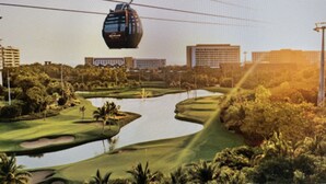 A cable car moving over a scenic landscape with a river, greenery, and buildings in the background. -  Vidanta Nuevo Vallarta! (Nuevo Vallarta)