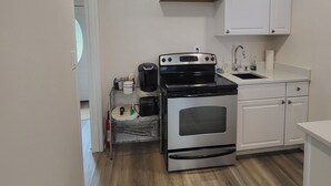 Une cuisine de taille réduite avec des meubles blancs, un four en acier inoxydable, une cuisinière noire et un évier.