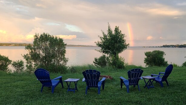 Une vue sur le lac avec des chaises et une table, un arc-en-ciel et des arbres.