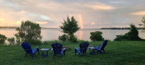 A lakeside view with chairs and a table, a rainbow, and trees. - Bright and airy waterfront getaway (Benedict)