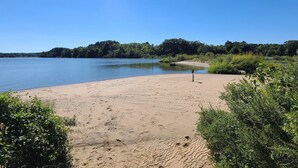 Une plage de sable où l’on peut voir des empreintes de pas, bordée de verdure et baignée par une étendue d’eau calme.