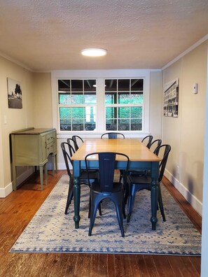 Un coin repas avec une table et des chaises en bois, un tapis et une fenêtre donnant sur un paysage verdoyant.