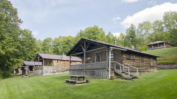A rustic log cabin with a porch and a picnic table, surrounded by lush greenery. - Mountain Lake Cottages (Orleans)