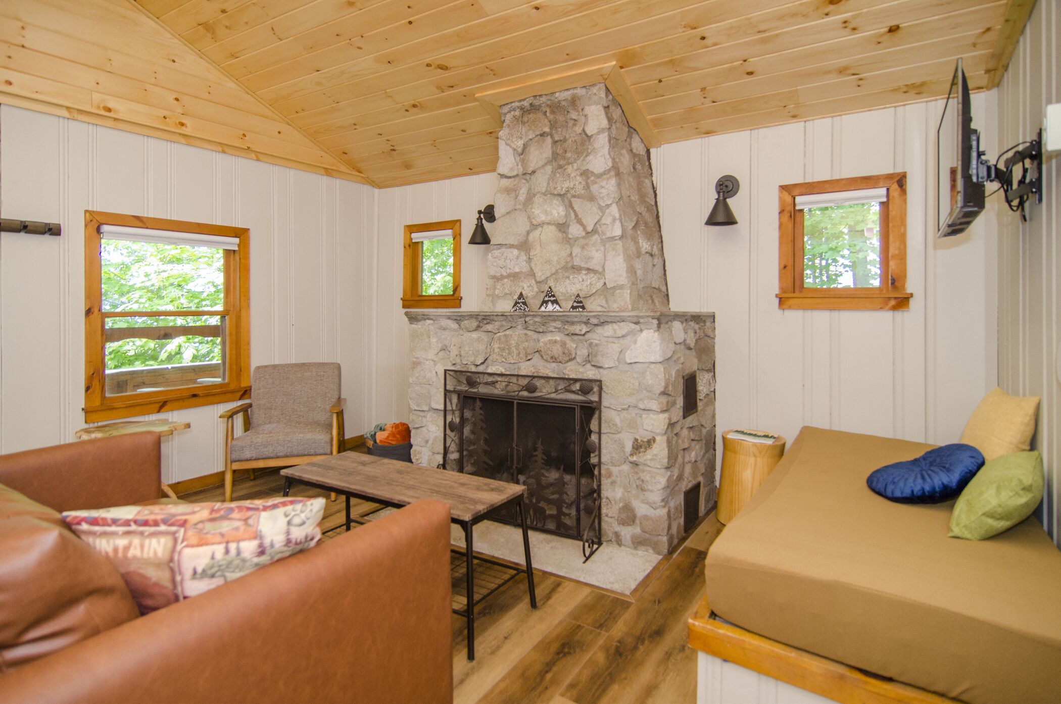 A cozy room with a stone fireplace, wooden ceiling, and a sofa with cushions.