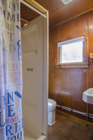 A wooden-paneled bathroom with a white toilet, a window above the sink, and a shower curtain with text. - Mountain Lake Cottages (Orleans)