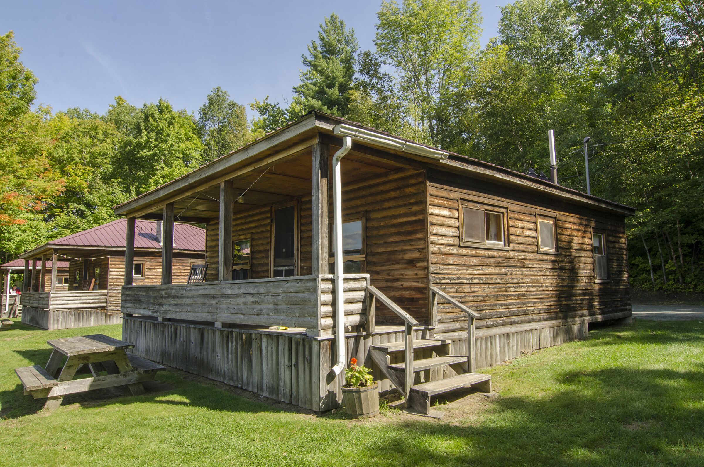A rustic wooden cabin with a porch, a picnic table, and a small garden area.