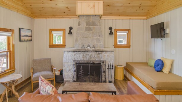 Una sala de estar acogedora con chimenea de piedra, techo de madera y un área de descanso confortable con sofá y banco.