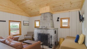 Acogedor interior de cabaña con chimenea de piedra, techo de madera y un sofá con cojines.
