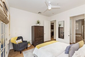 Una camera da letto con un letto, una poltrona scura, un armadio, una ventola a soffitto e l'accesso al bagno.