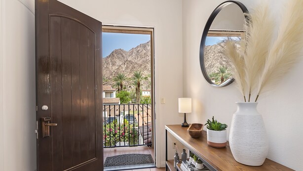 Une porte en bois sombre qui donne sur un balcon offrant une vue sur les montagnes et les palmiers.