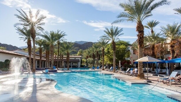 Une piscine bordée de palmiers, avec des chaises longues et une vue sur les montagnes en arrière-plan.