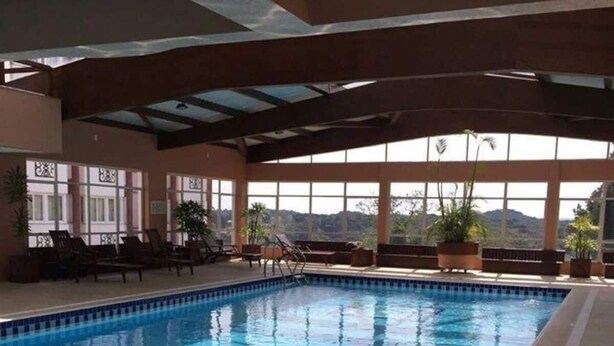 An indoor swimming pool with clear blue water, surrounded by lounge chairs and potted plants. - Apartment with heating and heated pool near the city center! (RS)