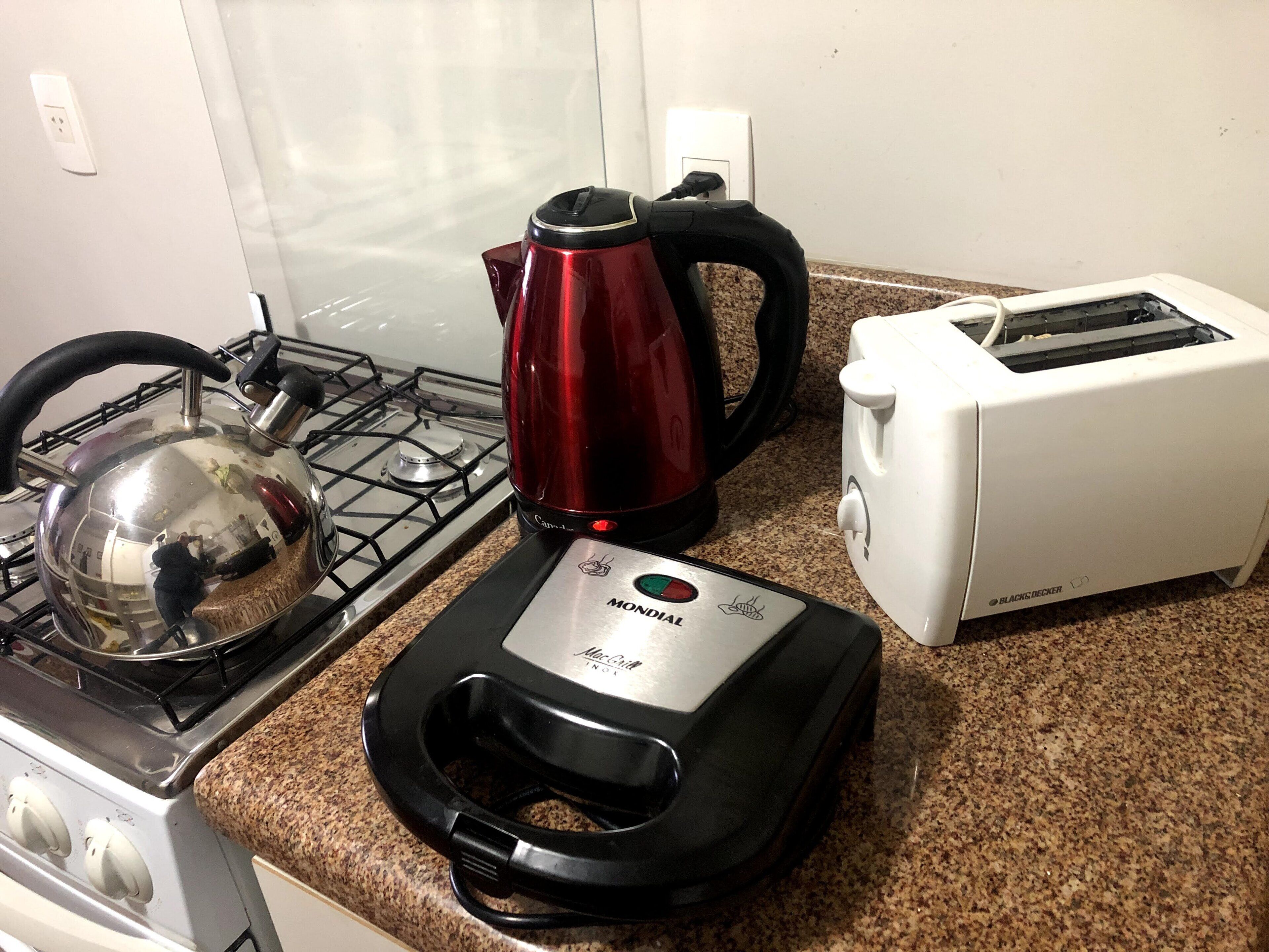 A kitchen with a gas stove, a red kettle, a toaster, and a coffee maker.