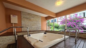 A hot tub in a room with a stone wall and a window with a view of pink flowers. - Apartment with heating and heated pool near the city center! (RS)