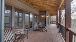 Une véranda couverte avec un plancher en bois, de grandes fenêtres et des sièges d’extérieur.