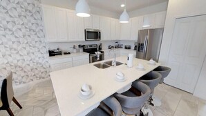 A modern kitchen with white cabinets, a central island with stools, stainless steel appliances, and pendant lighting.