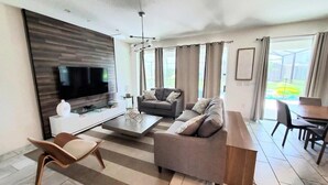 A modern living room with a flat-screen TV, a sofa, a coffee table, and a dining area with a table and chairs.