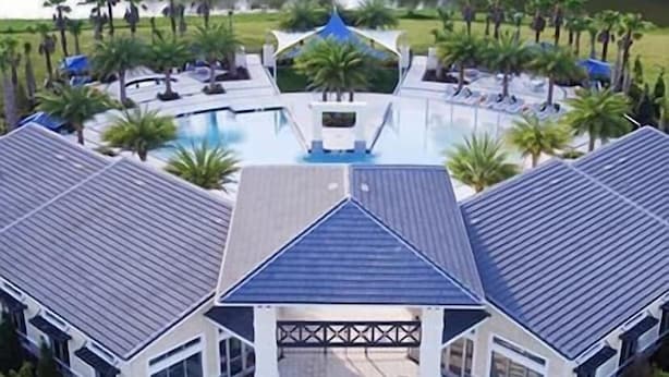 A large building with a central pool, surrounded by palm trees and a lake.