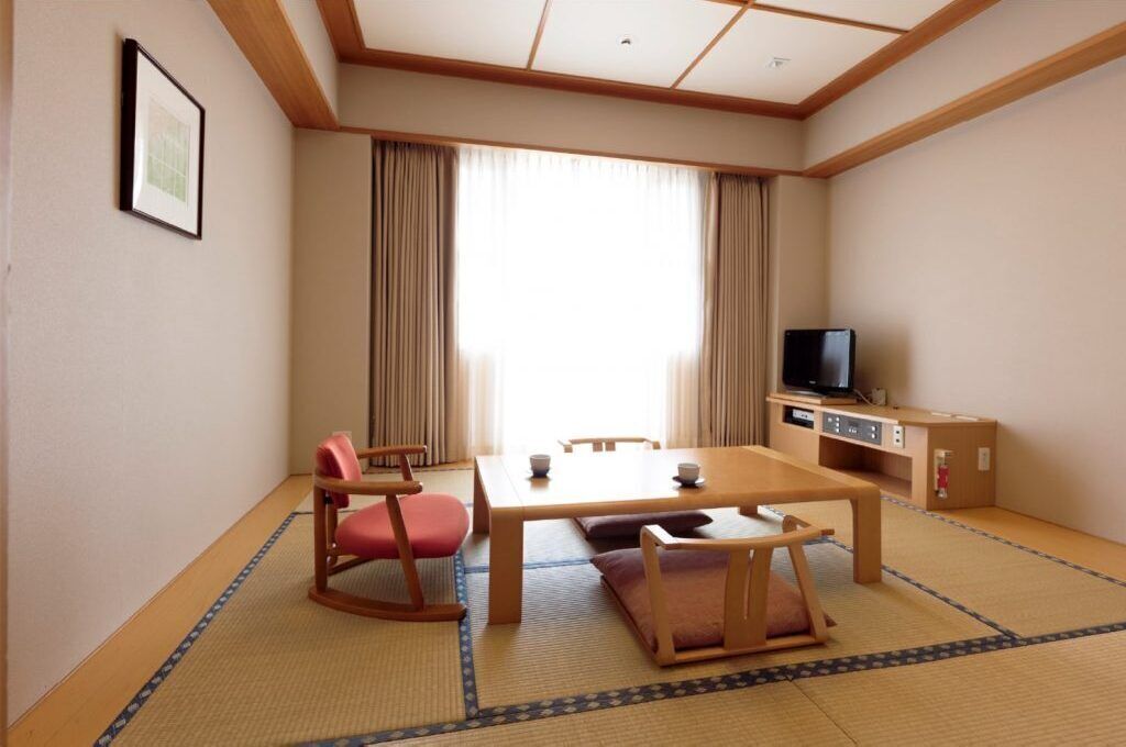 A traditional Japanese room with tatami flooring, a low table, chairs, a television, and a framed picture on the wall.