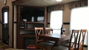 A dining area with a wooden table and chairs, a television, and a fireplace. - A Country Escape (Ayden)