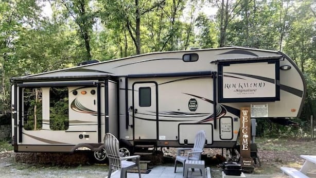 A recreational vehicle with a 'Rockwood Signature' sign, a covered area with chairs, and a 'Welcome' sign. - A Country Escape (Ayden)