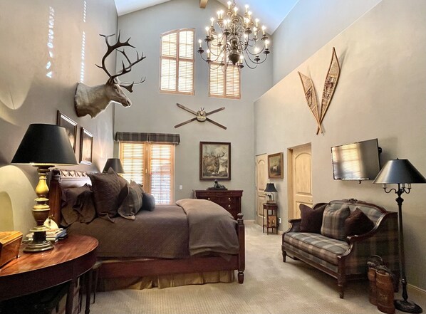 A spacious room with a large bed, a chandelier, and wall-mounted deer antlers.
