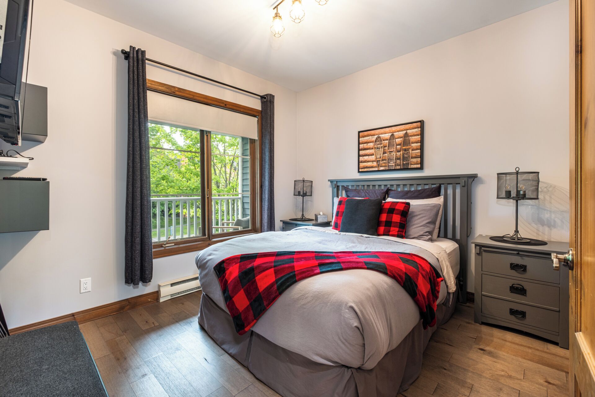 A bedroom with a bed, a nightstand, a dresser, a window with curtains, and a ceiling light.