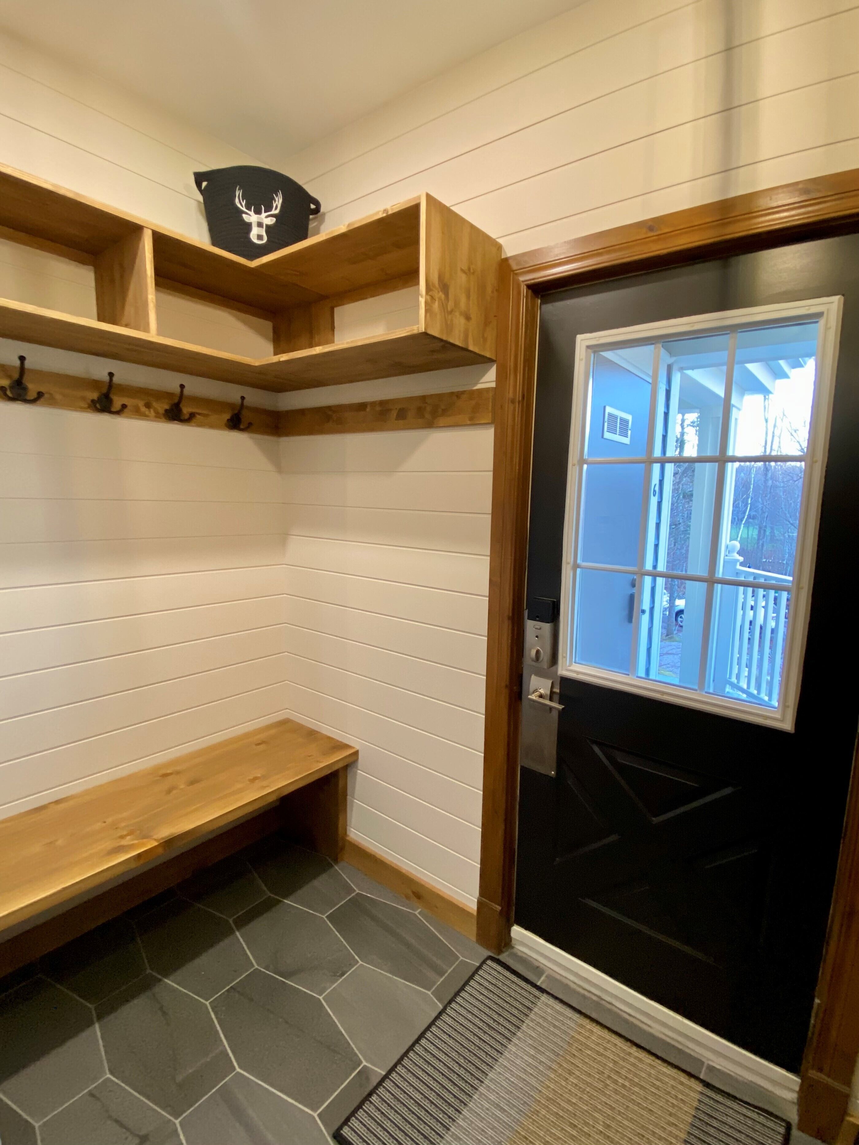 A room with a bench, wooden shelves, a door with a window, and a stone-patterned floor.