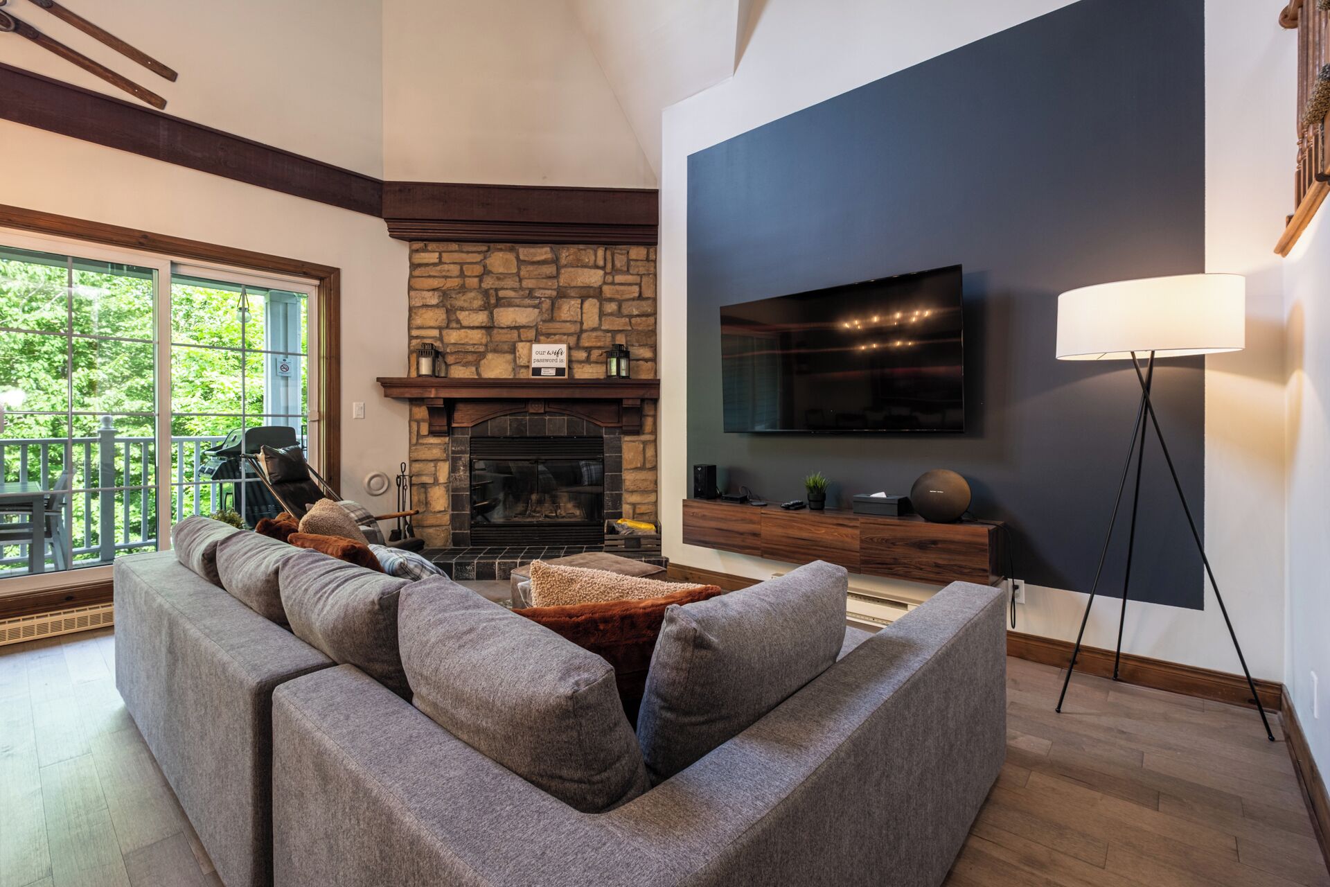 A modern living room with a stone fireplace, a large flat-screen TV, and a cozy seating area.