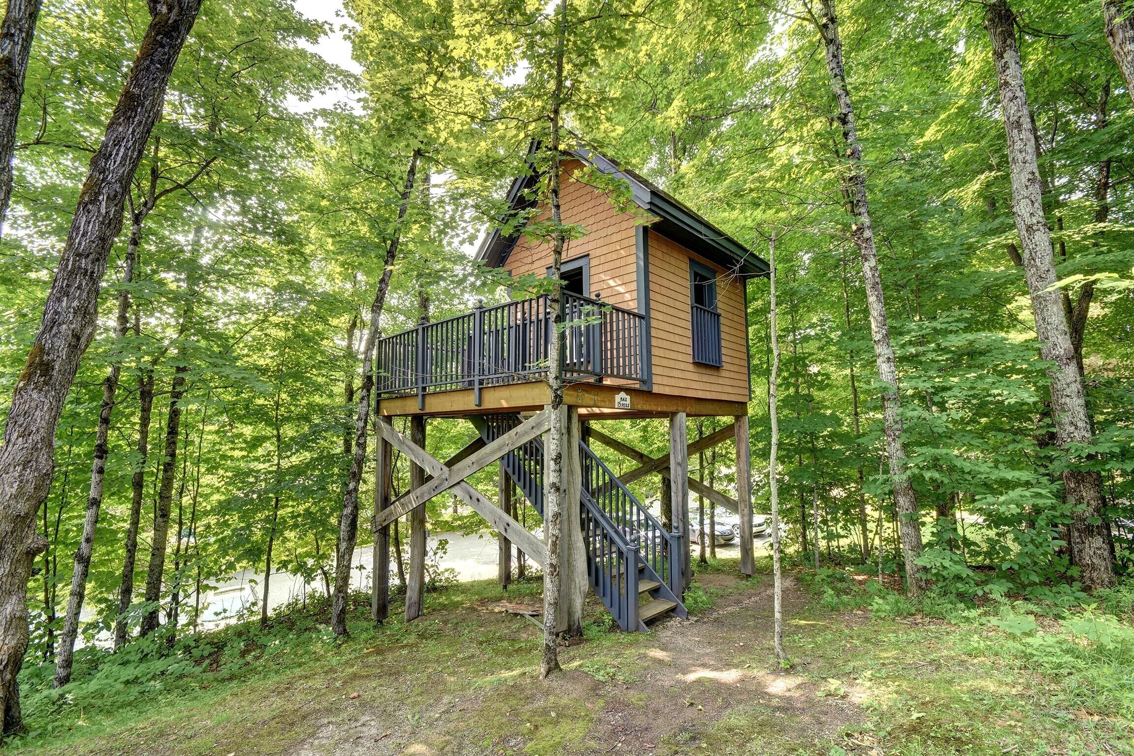 A wooden treehouse with a balcony and stairs, surrounded by a forest.