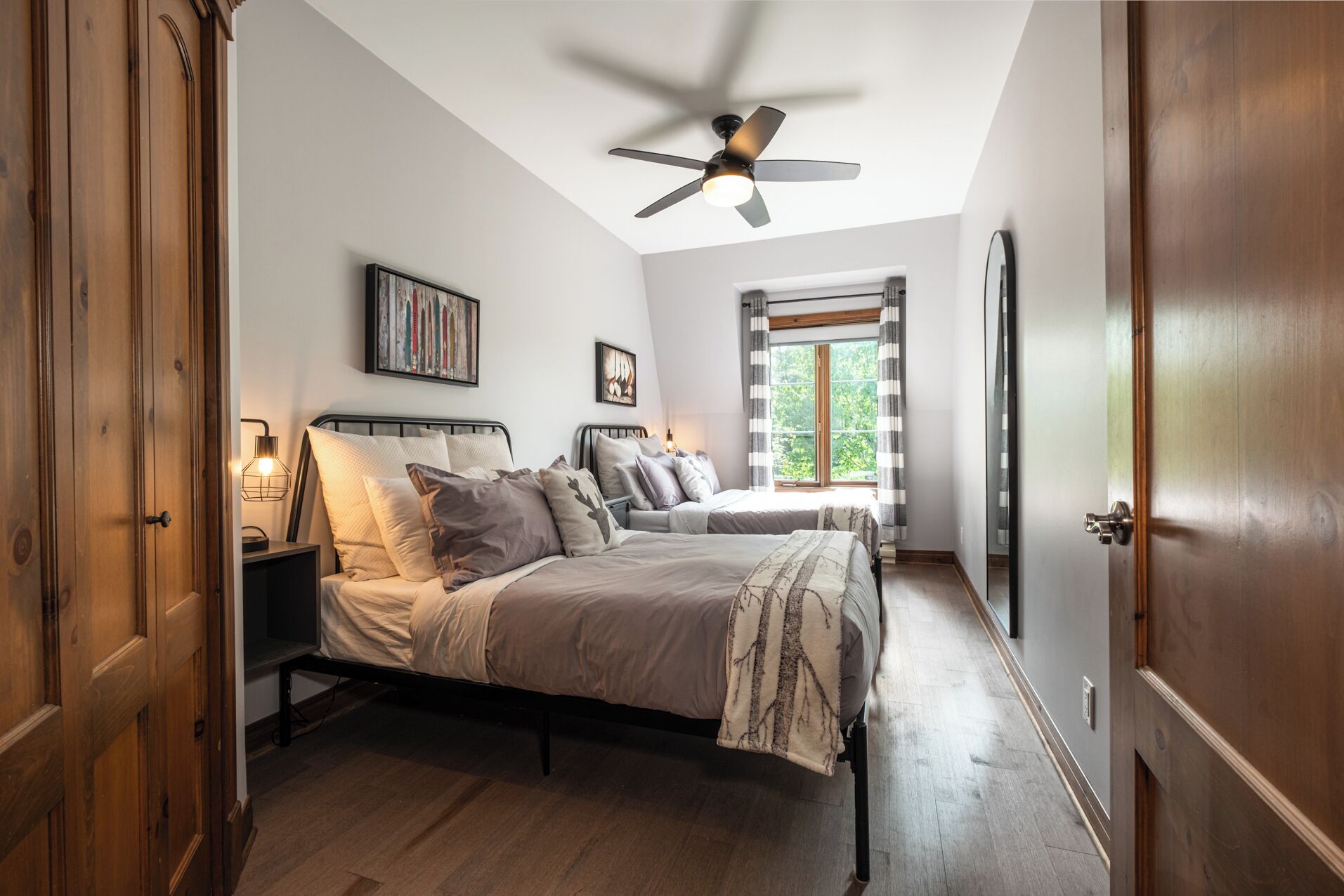 A bedroom with a bed, bedside tables, a ceiling fan, a window with curtains, and a door.