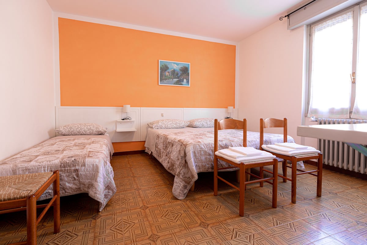 A dormitory room with two beds, a radiator, and a window with curtains.