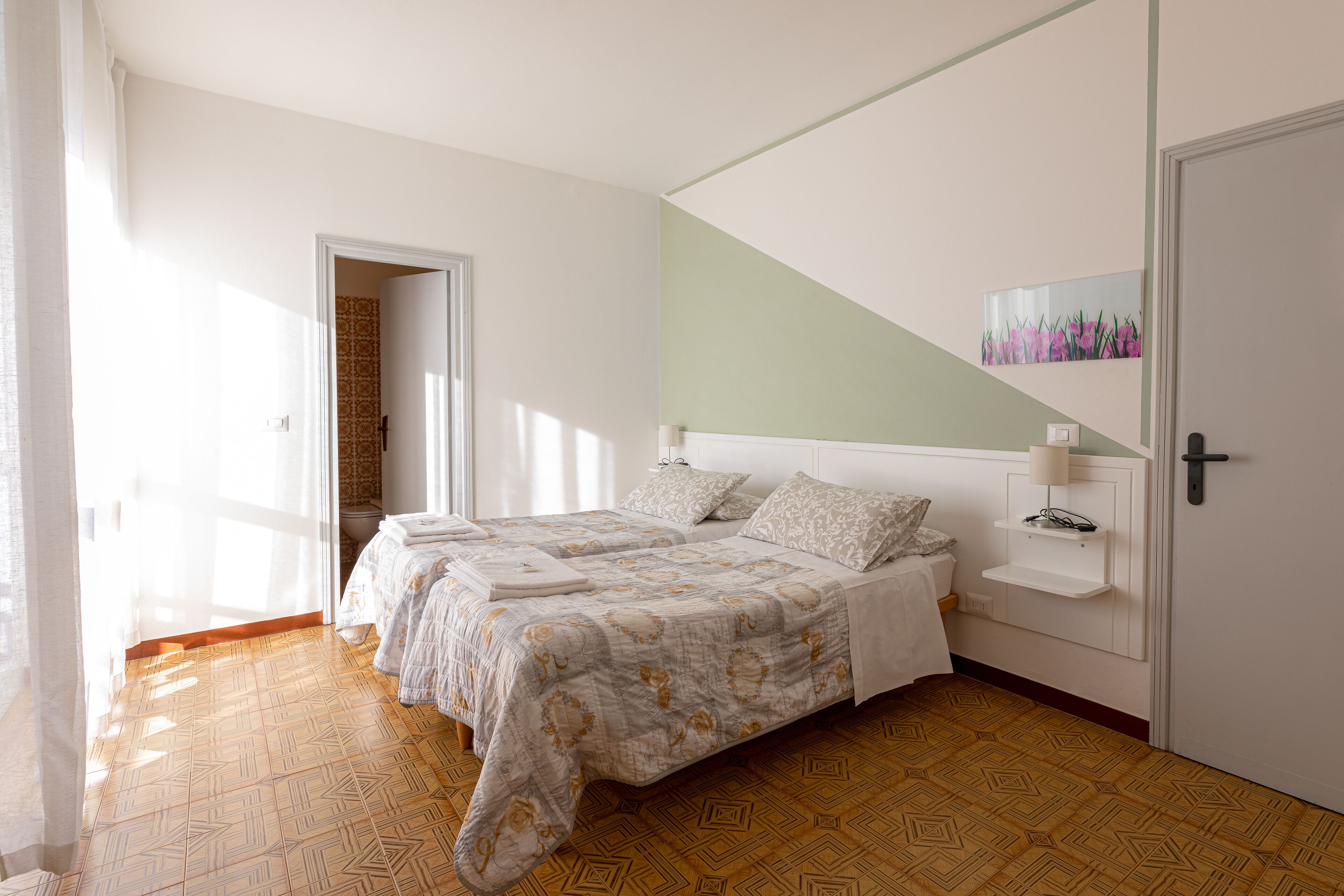 Ein Doppelbett mit gemustertem Überwurf, ein Nachttisch mit Lampe und ein an der Wand befestigtes Regal.