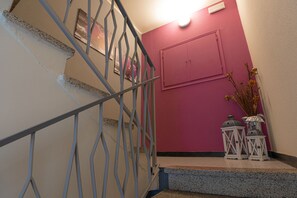 A staircase with a metal railing, a pink wall, and two white lanterns on the landing. - La Svolta (Chiuro)