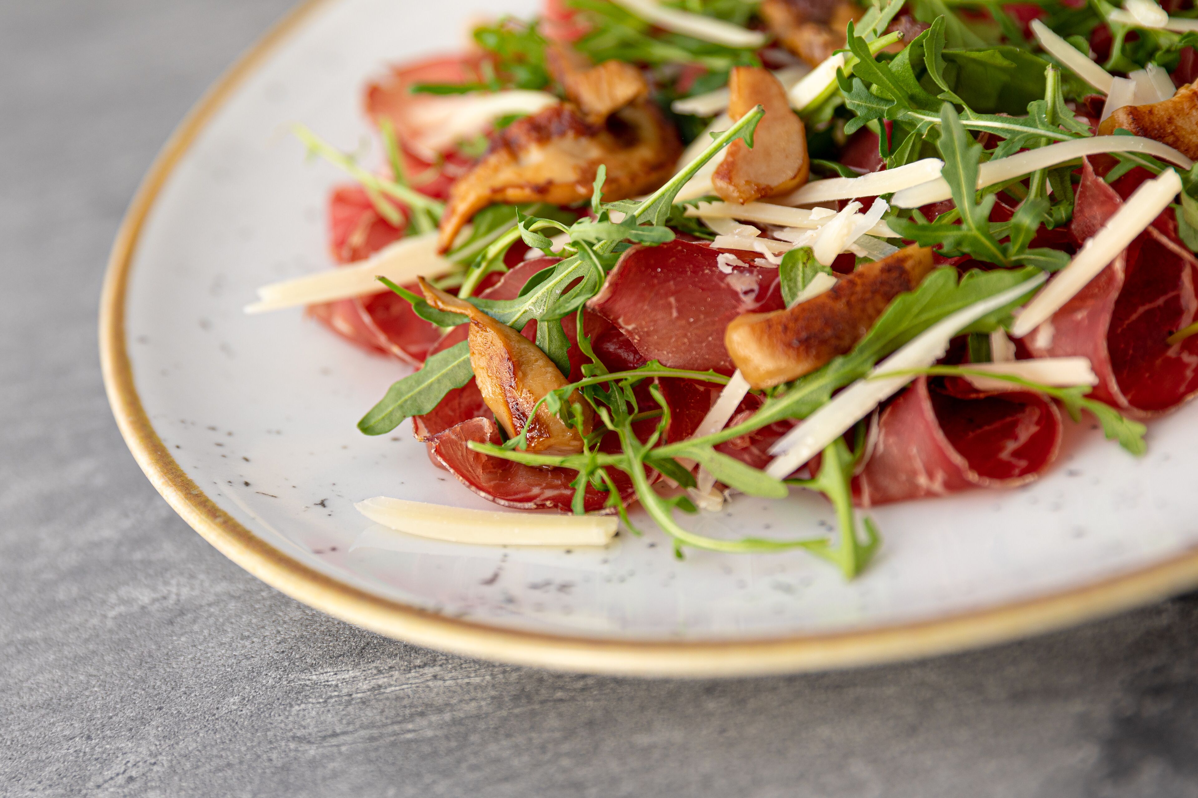 A plate of food with arugula, prosciutto, and shaved cheese.