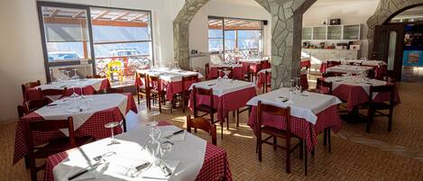 A restaurant with red and white checkered tablecloths, stone arches, and wooden flooring.