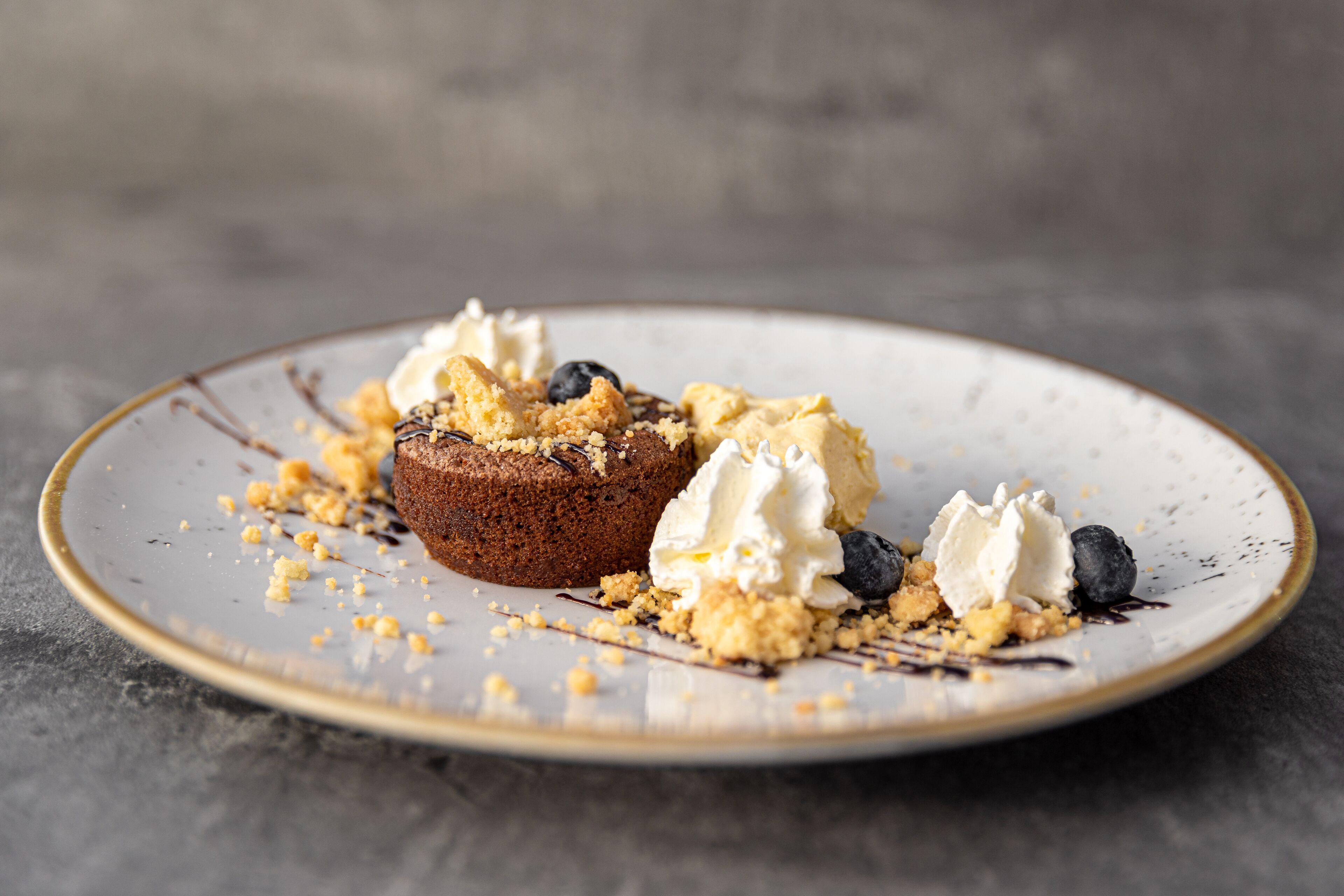A dessert on a plate with a crumbly topping, a scoop of ice cream, and a blueberry.