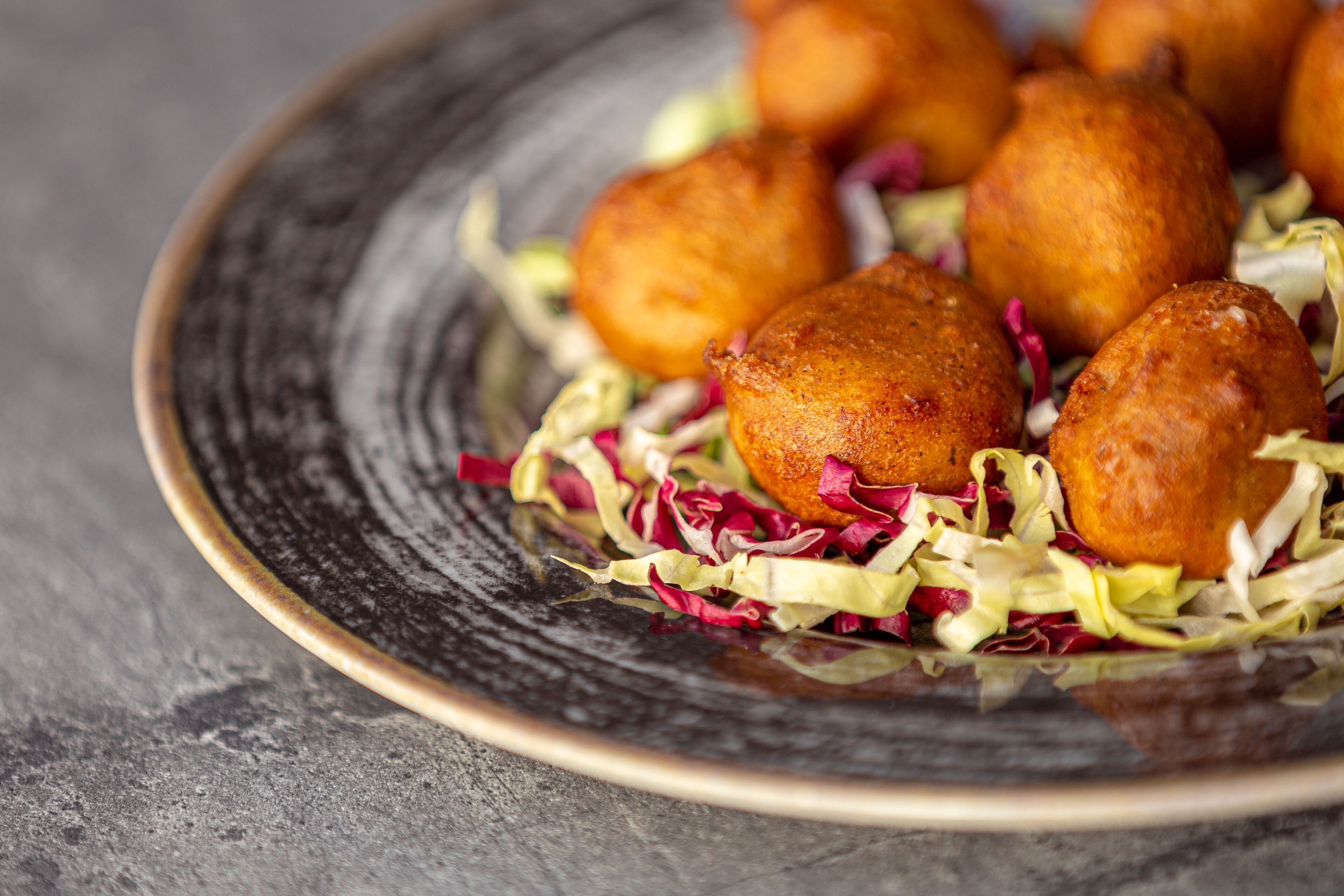 Ein Teller mit goldbraunen, frittierten Speisen, gewürfeltem Weißkohl und Rotkohl auf einer strukturierten Keramikplatte.
