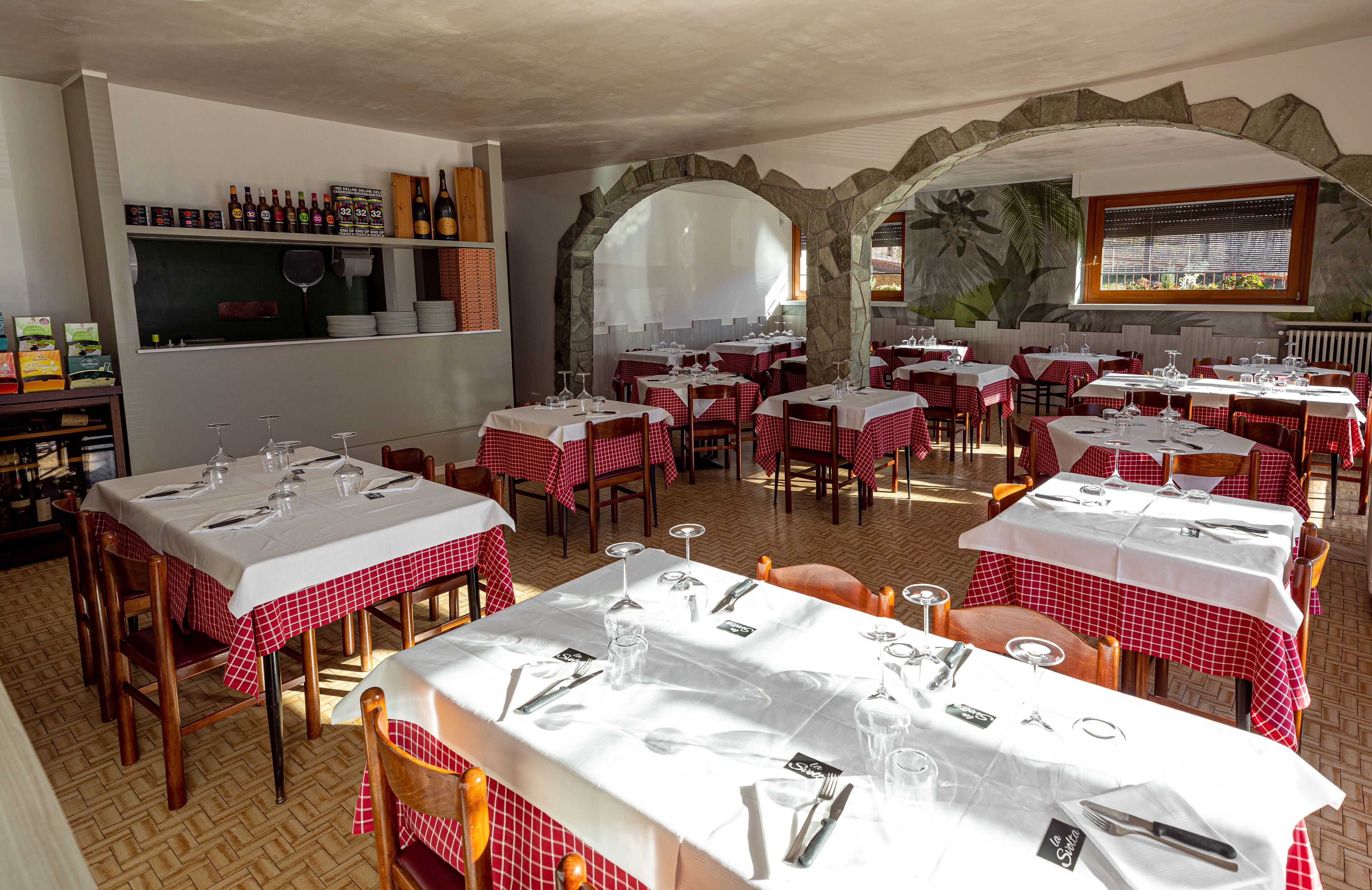 A restaurant with tables set for dining, a wine rack, and a mural on the wall.