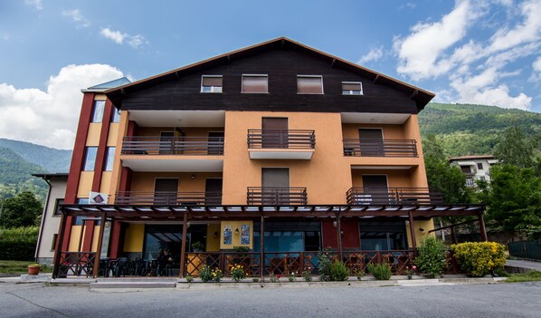 A multi-story hotel with balconies, a covered outdoor seating area, and a mountain backdrop. - La Svolta (Chiuro)