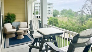 A covered porch with wicker furniture, a blue rug, and a view of a building and greenery.