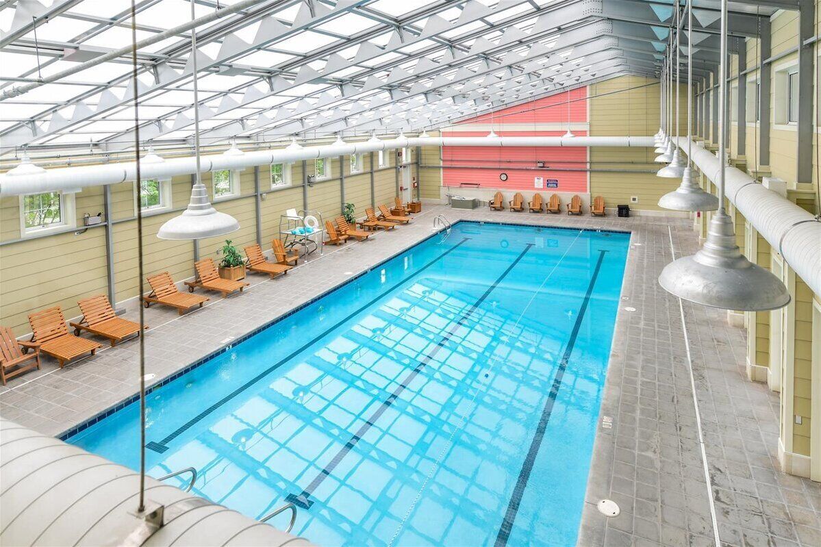 Une piscine intérieure dotée de plusieurs couloirs de nage, de chaises longues et d’un haut plafond agrémenté de lucarnes.