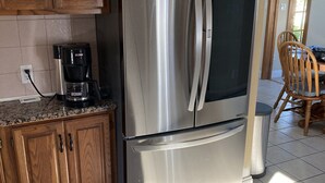 Cozinha com armários de madeira, geladeira de aço inoxidável, máquina de café e área de jantar com cadeira e mesa.