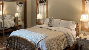 Quarto com cama de madeira, mesa de cabeceira com abajur, espelho e janela com cortinas.