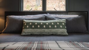 Una cama con cabecera acolchada, dos almohadas y vistas a árboles por la ventana.