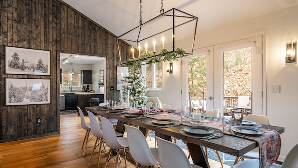 Un comedor con una mesa de madera dispuesta para cuatro personas, rodeada de sillas blancas, y una araña colgante.