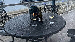 Ein runder Tisch mit zwei Weingläsern und einer Flasche auf einer Terrasse mit Blick auf ein Gewässer.